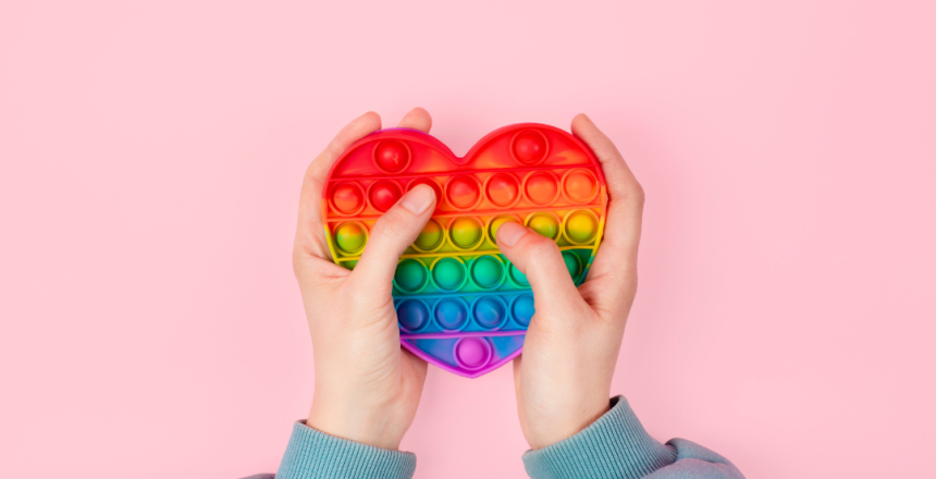 Hands holding a rainbow heart-shaped stim toy, symbolising comfort and the personal process of self-identifying as autistic.